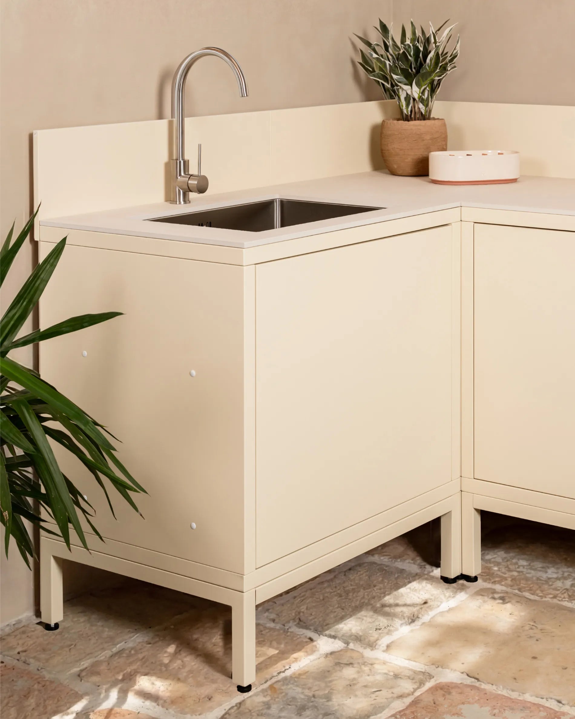 Crèmekleurige beige onderstructuur PILOTIS onder hoekkast met spoelbak, buitenkeuken met kraan en plant