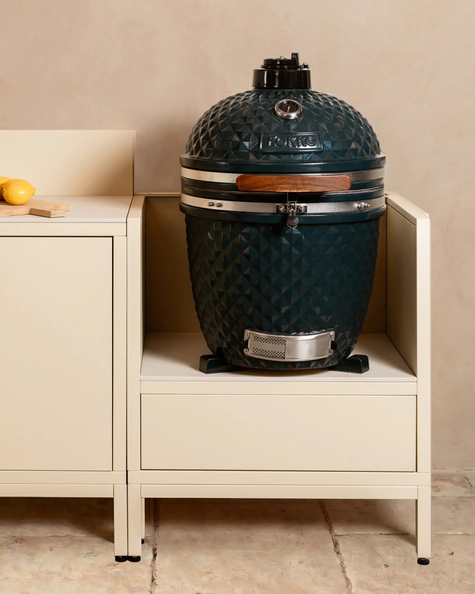 Marineblauwe Kokko kamado barbecue geplaatst in een crèmekleurige PILOTIS buitenkeukenmodule