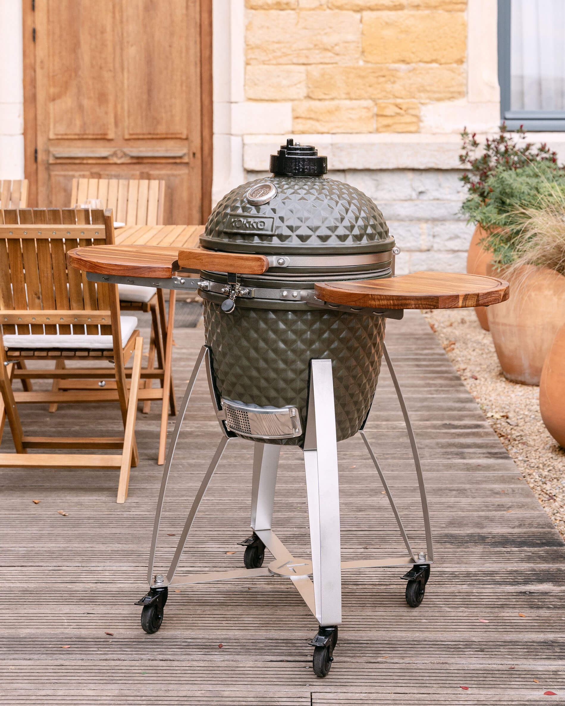 Kamado Kokko op een verrijdbaar onderstel met houten zijtafels, gepresenteerd buiten op een terras.