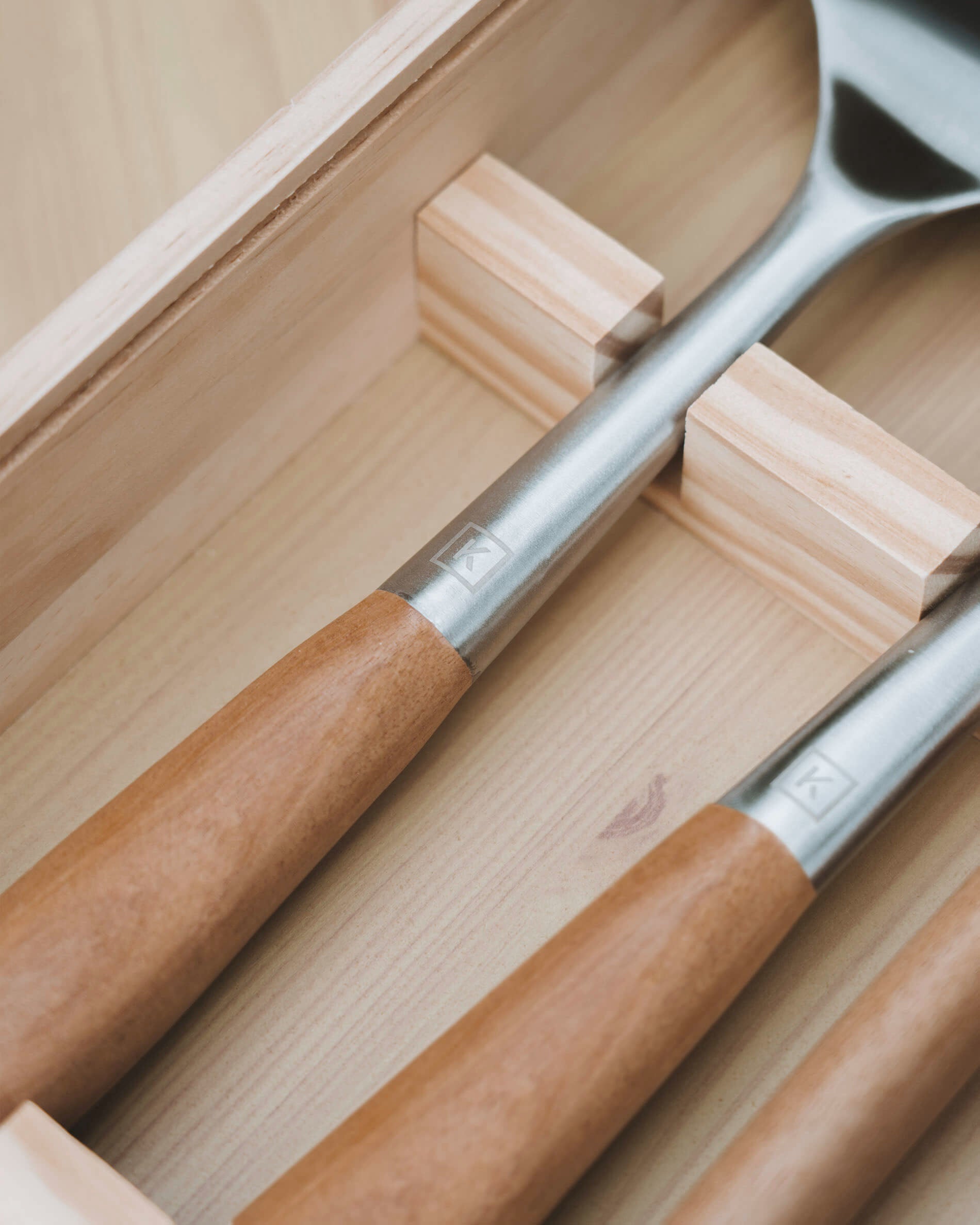Detail van keukengerei met handgrepen van acaciahout en koppen van roestvrij staal, netjes opgeborgen in een houten kist met vakverdeling