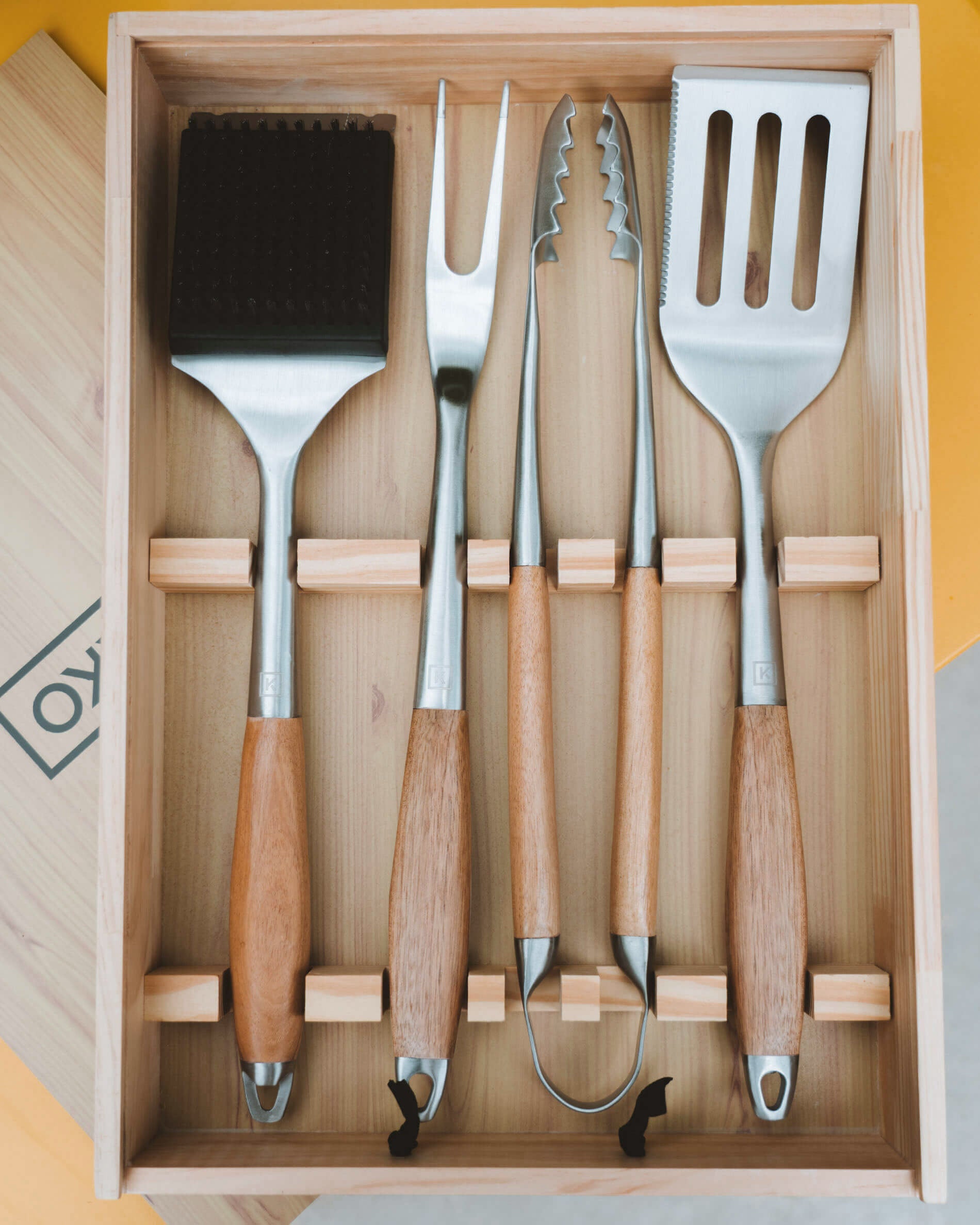 Bovenaanzicht van een houten kist met een set roestvrijstalen keukengerei met acaciahouten handgrepen, netjes opgeborgen in vakken.