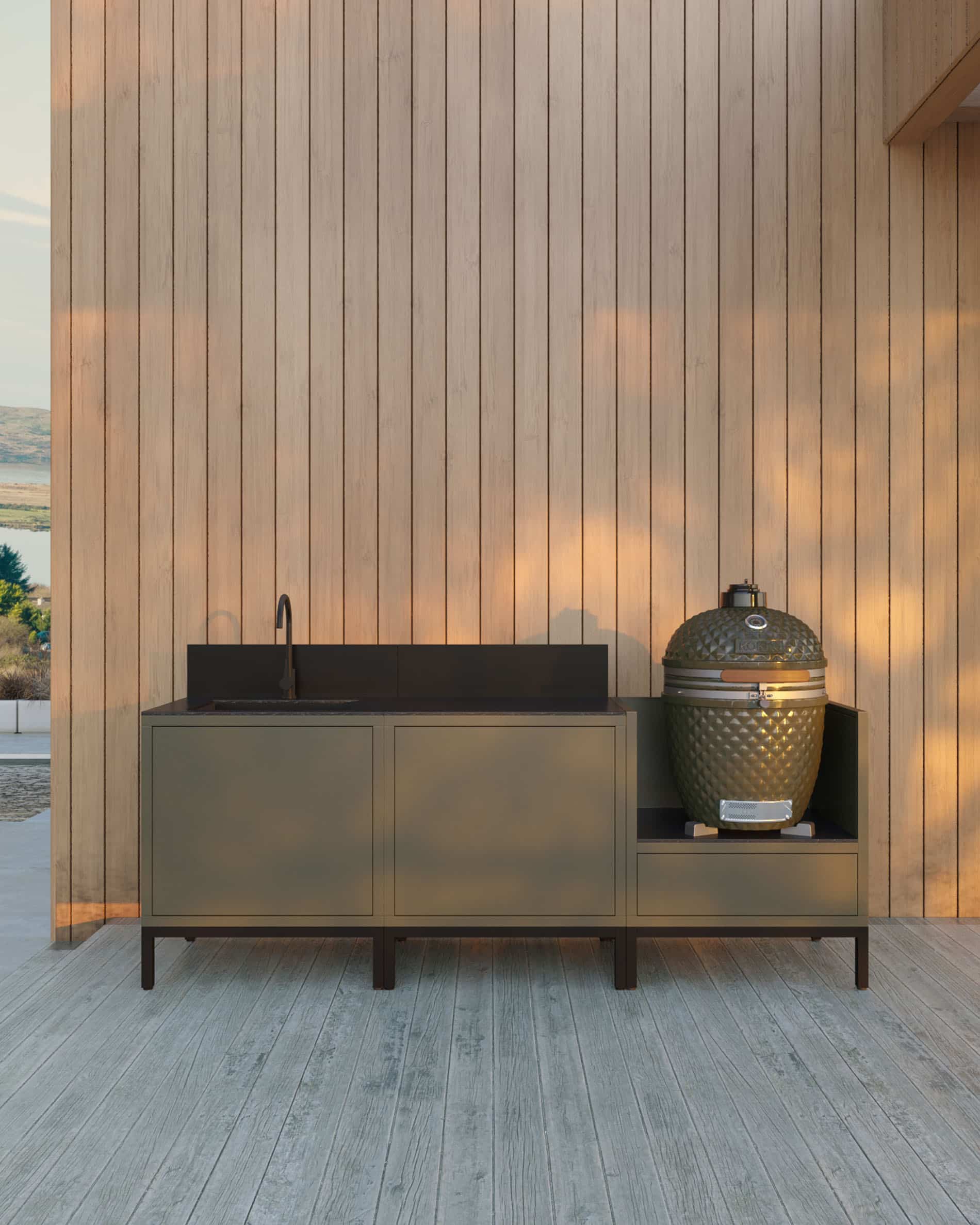 Buitenkeuken op palen met 3 modules voor kamado, geïntegreerde spoelbak, meubel in olijfgroen met bijpassend werkblad en achterwand, spoelbak met kraan links, twee gesloten opbergmodules in het midden en geïntegreerde kamado in de rechter zijmodule, constructie op zwarte poten, geplaatst buiten tegen een houten gevel.