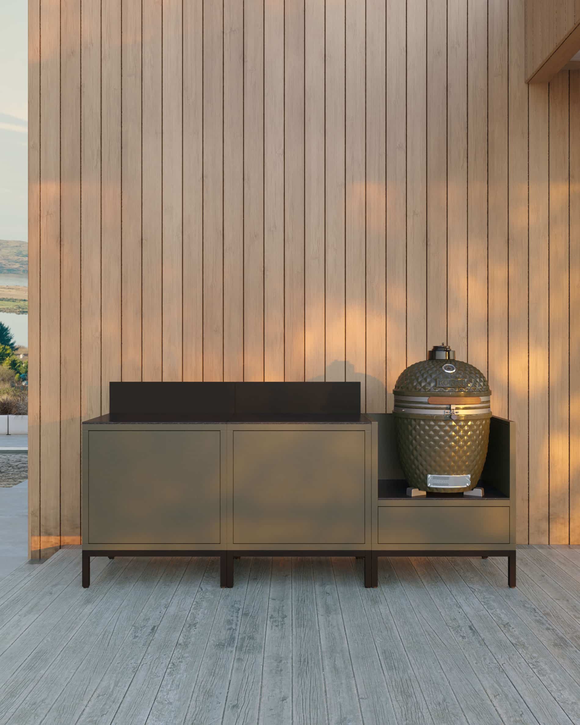 Buitenkeuken op palen met 3 modules voor kamado, meubel in olijfgroene kleur met donker werkblad en bijpassende achterwand, twee gesloten opbergmodules links en geïntegreerde kamado in de rechter zijmodule, constructie op zwarte poten, geplaatst buiten tegen een houten wand.