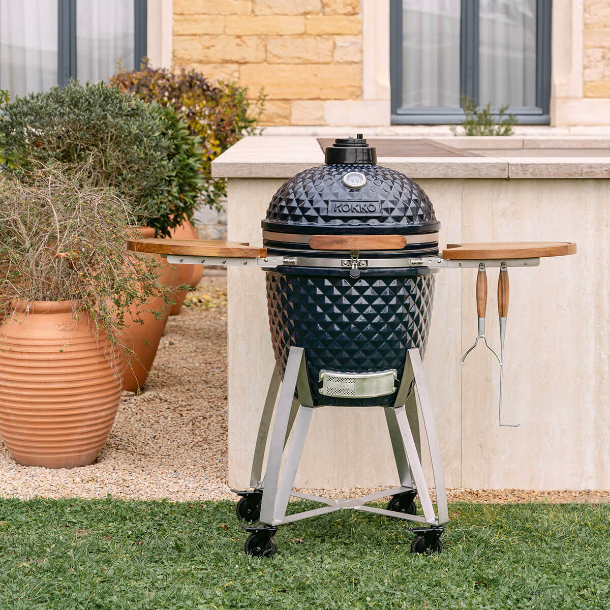 Kamado Kokko navy van keramiek, voorzien van houten zijtafels en een verrijdbaar onderstel met wielen.
