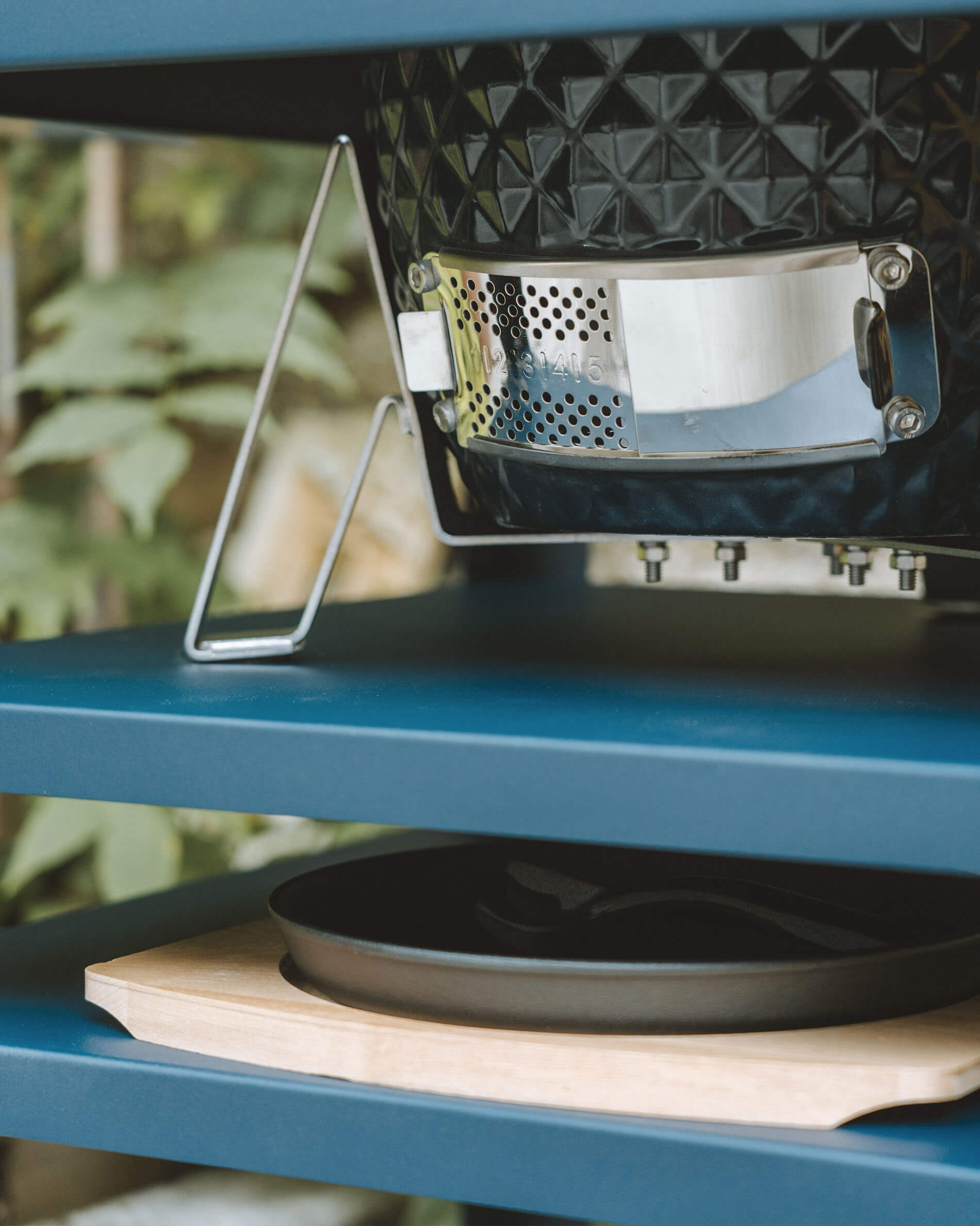 Close-up van de roestvrijstalen onderste ventilatie van een Kokko kamado, geïntegreerd in een metalen werktafel met asopvangbak.