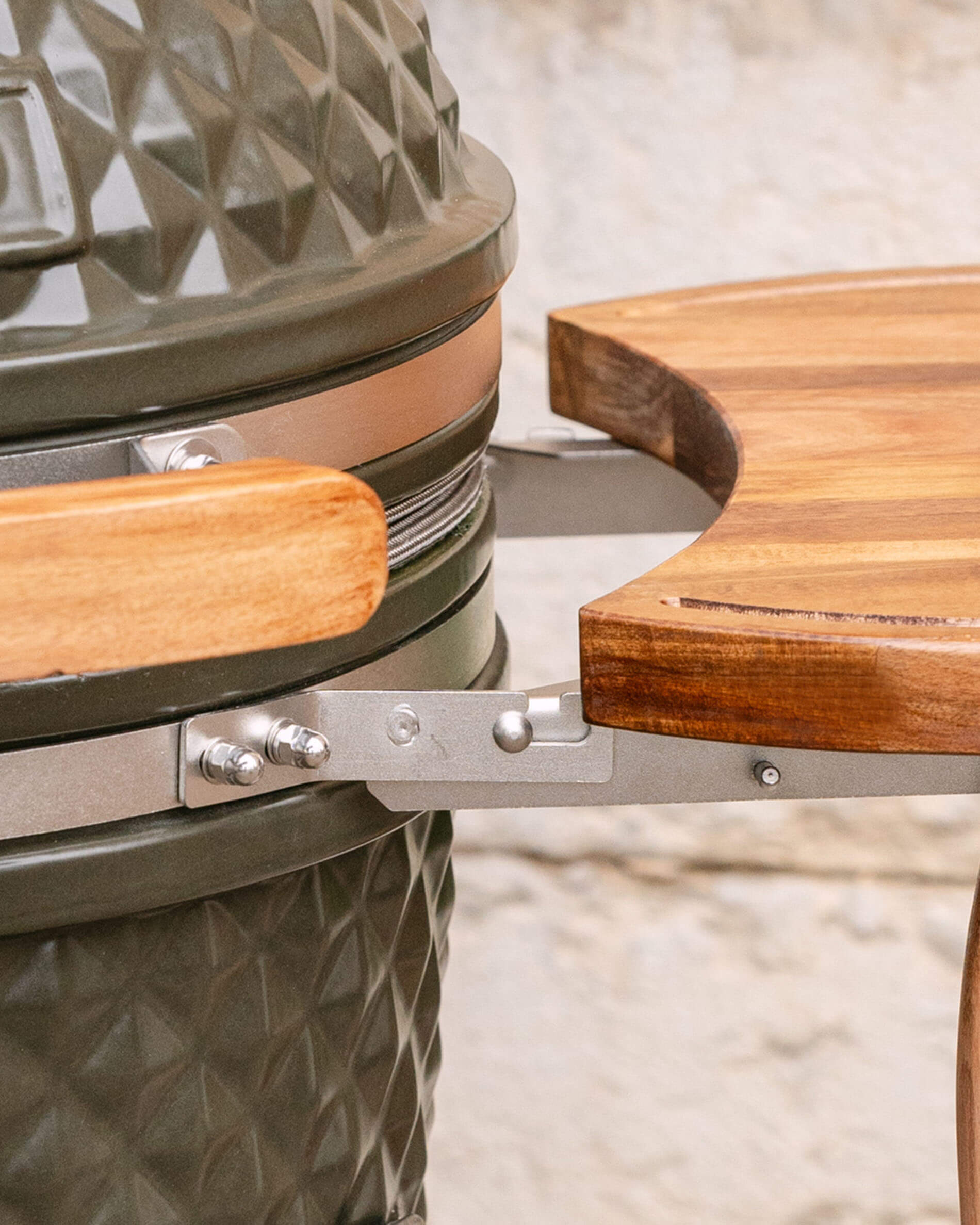 Close-up van de metalen bevestiging die het houten zijplateau met de kamado verbindt, met zicht op het bevestigingssysteem en het schroefwerk.