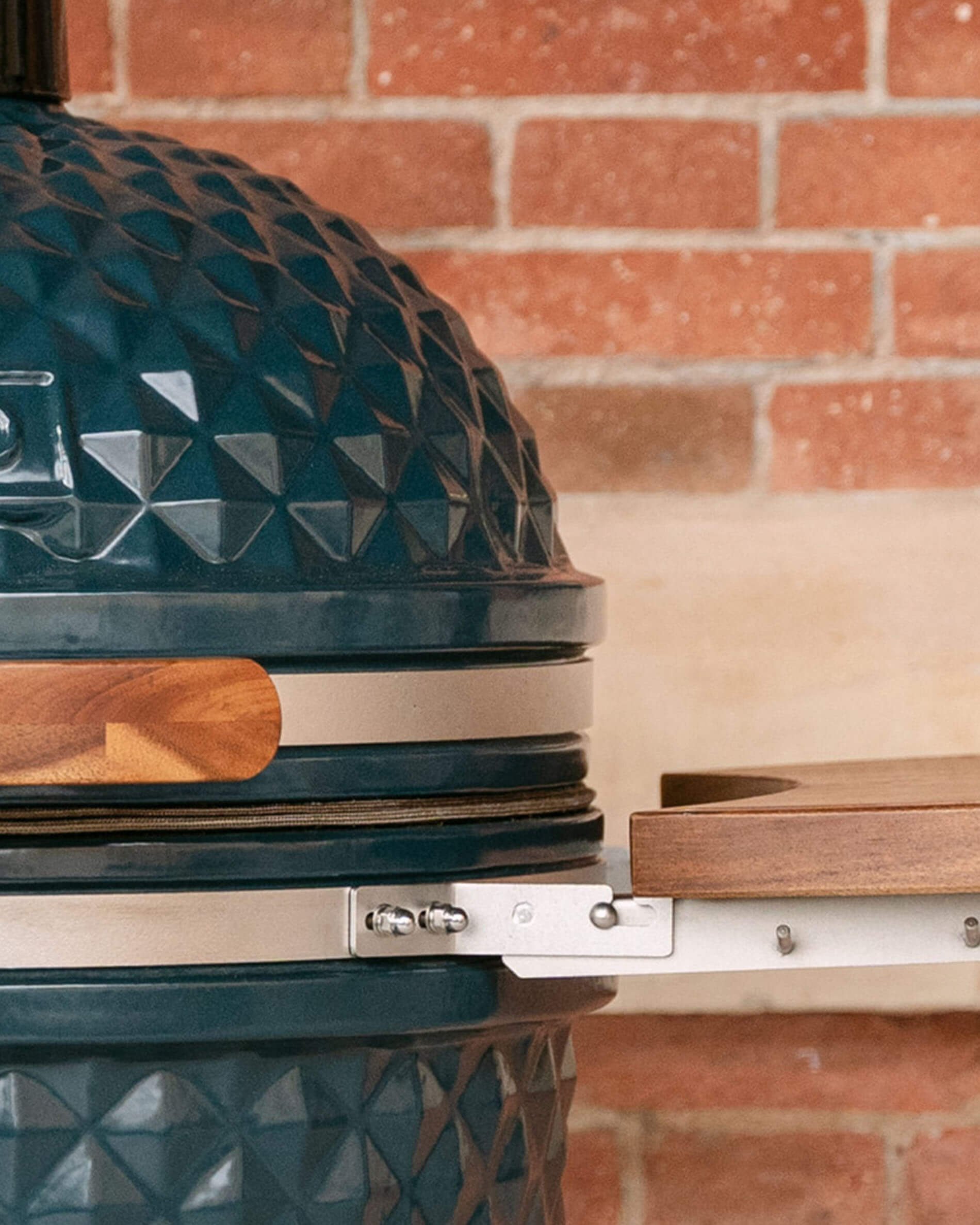 Detail van de metalen bevestigingen die een houten zijplank verbinden met de kamado, met zichtbare schroeven en een zichtbaar afdichtingsrubber.