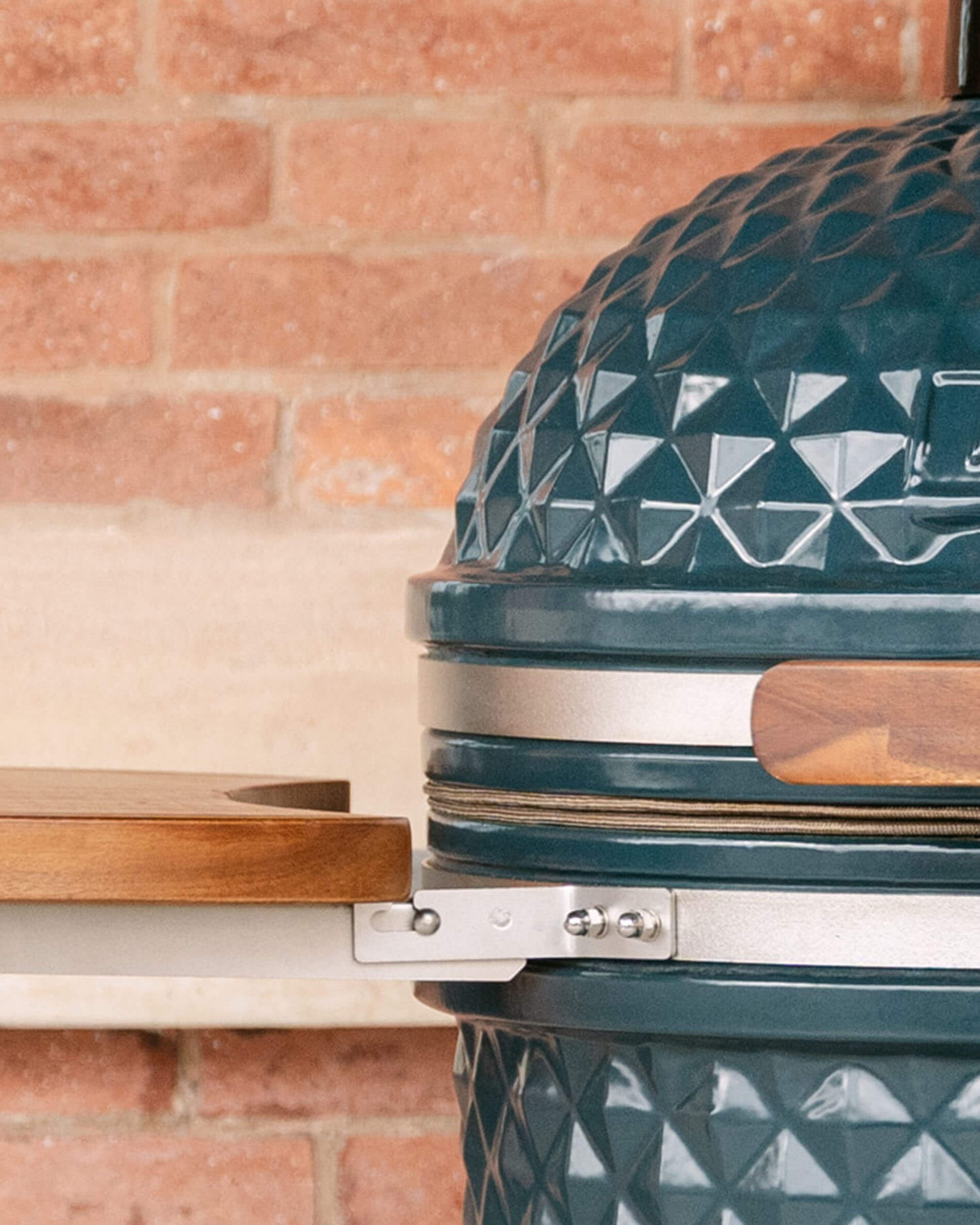 Detail van de zijkantbevestiging van een houten zijtafel op de Kokko kamado, met het metalen supportsysteem dat het plateau met de keramische kuip verbindt.