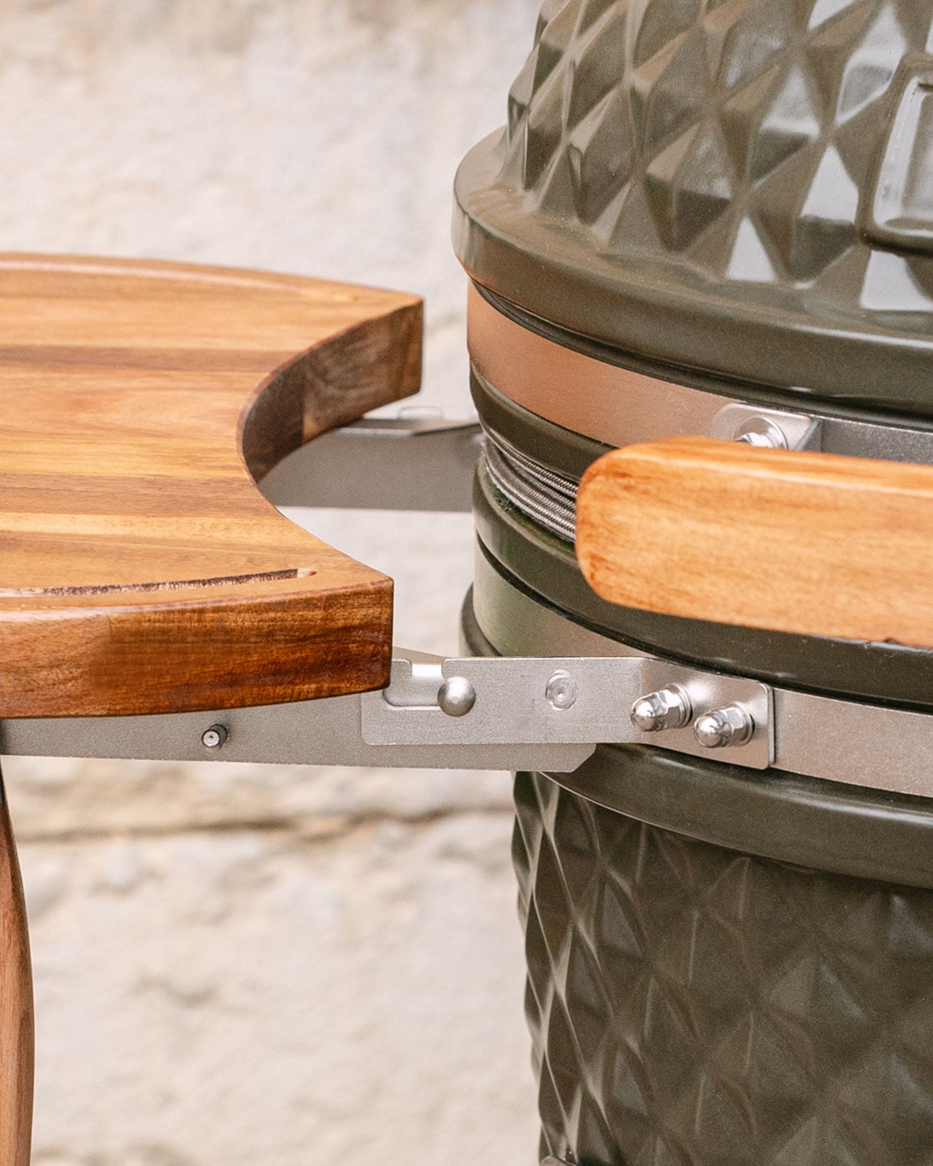 Detail van de metalen bevestigingen die het houten zijblad met de kamado verbinden, met zichtbare houten handgreep en roestvrijstalen omlijsting.