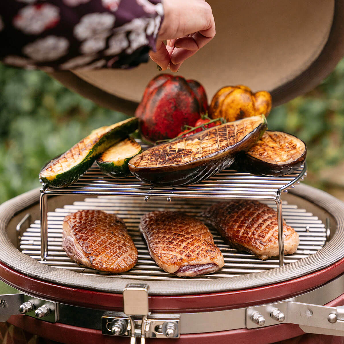 Twee-niveaus koken in een Kokko kamado met eendenborstfilets dichtgeschroeid op het onderste rooster en gegrilde groenten op het verhoogde rooster, als illustratie van veelzijdig koken.