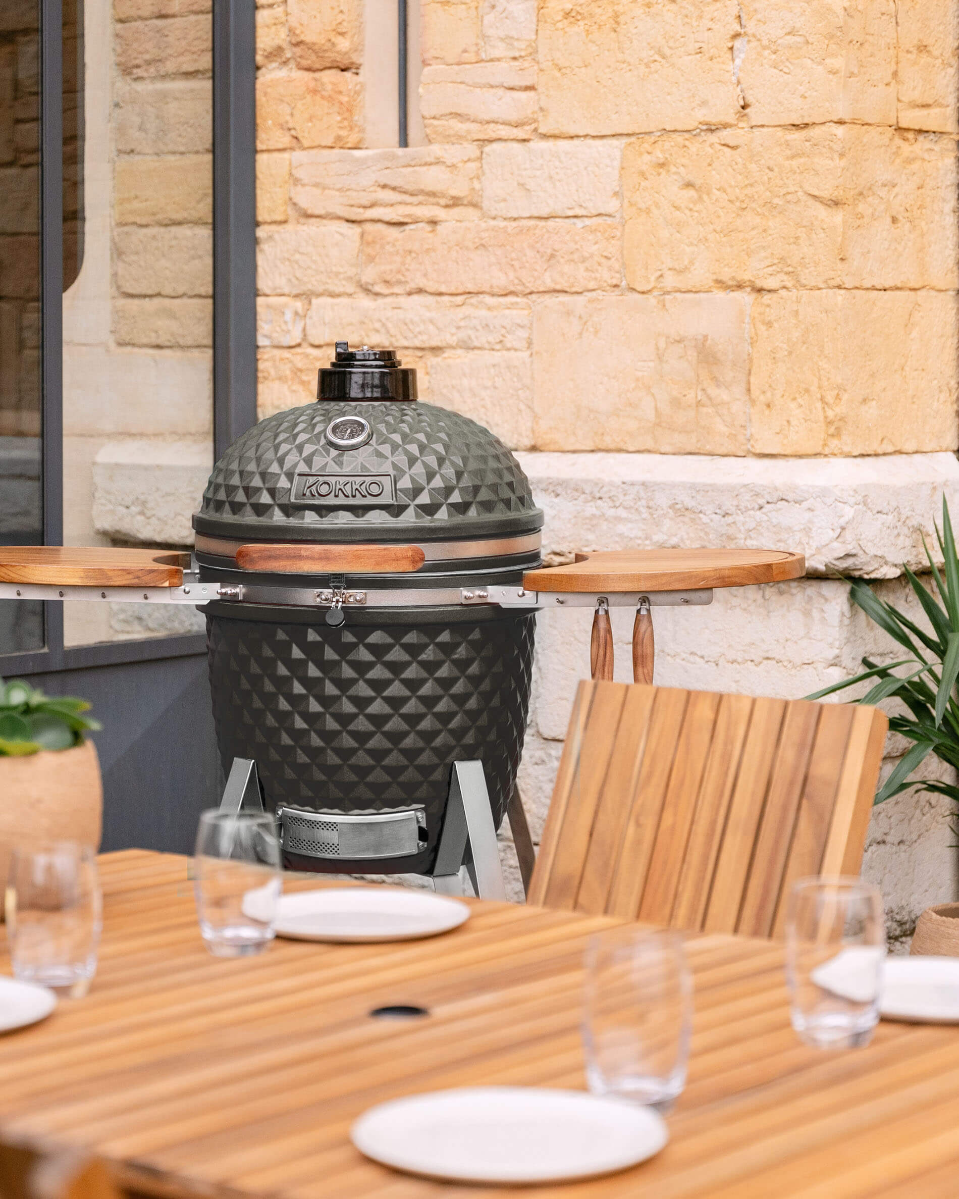 Kamado Kokko 22 inch in olijfgroen keramiek gepresenteerd op een terras.