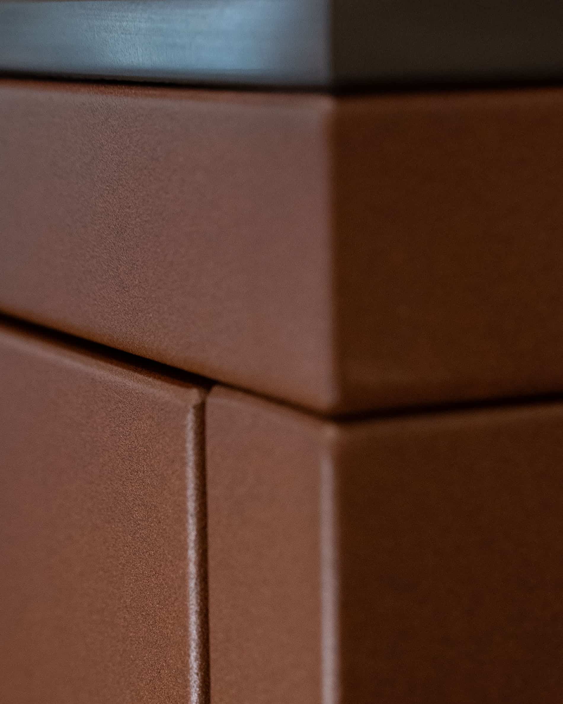 Detail van de afwerking van een pilotis buitenkeuken, met de hoek van het meubel, de aansluiting van de panelen en de matte textuur van het roestbruine front.