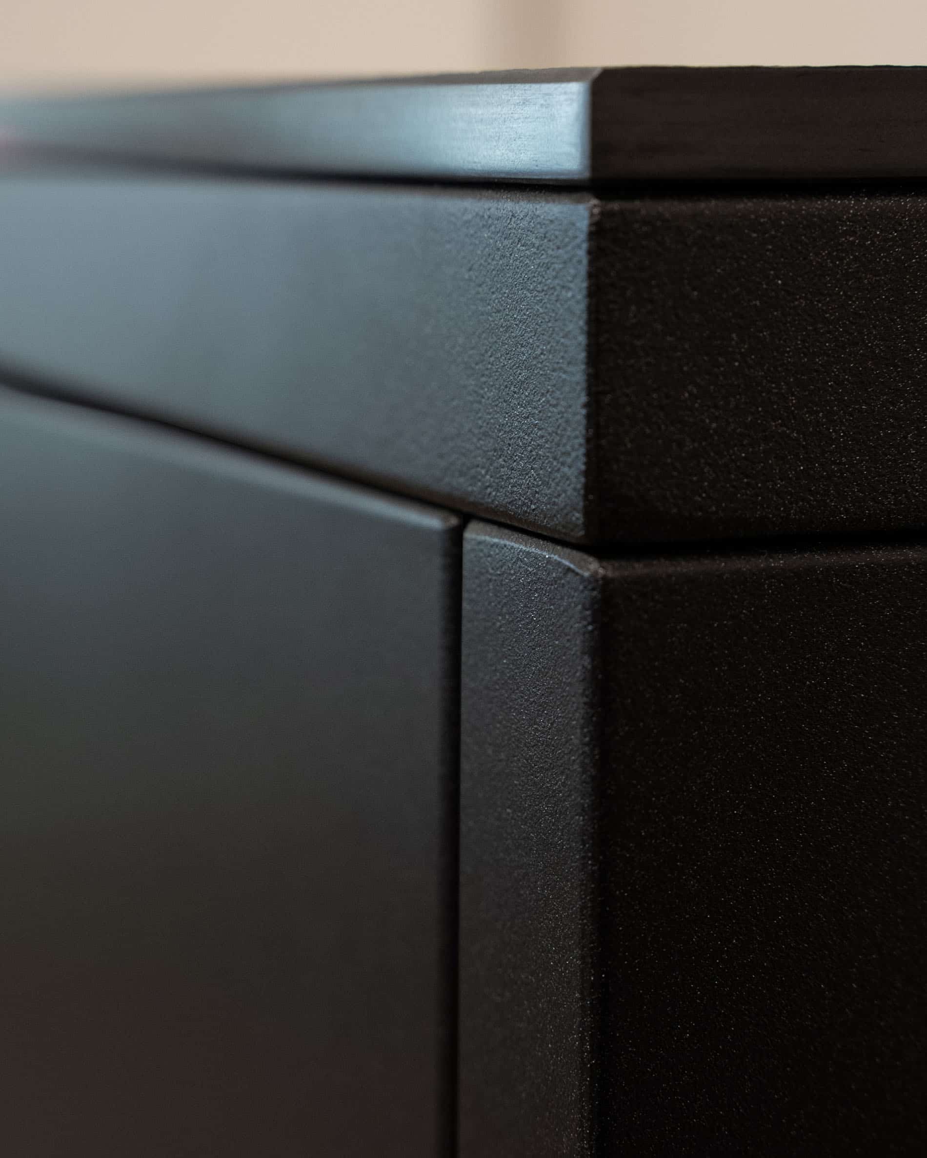 Detail van de afwerking van een pilotis-buitenkeuken, met de hoek van het meubel, de aansluiting van de panelen en de matte textuur van het donkere front.