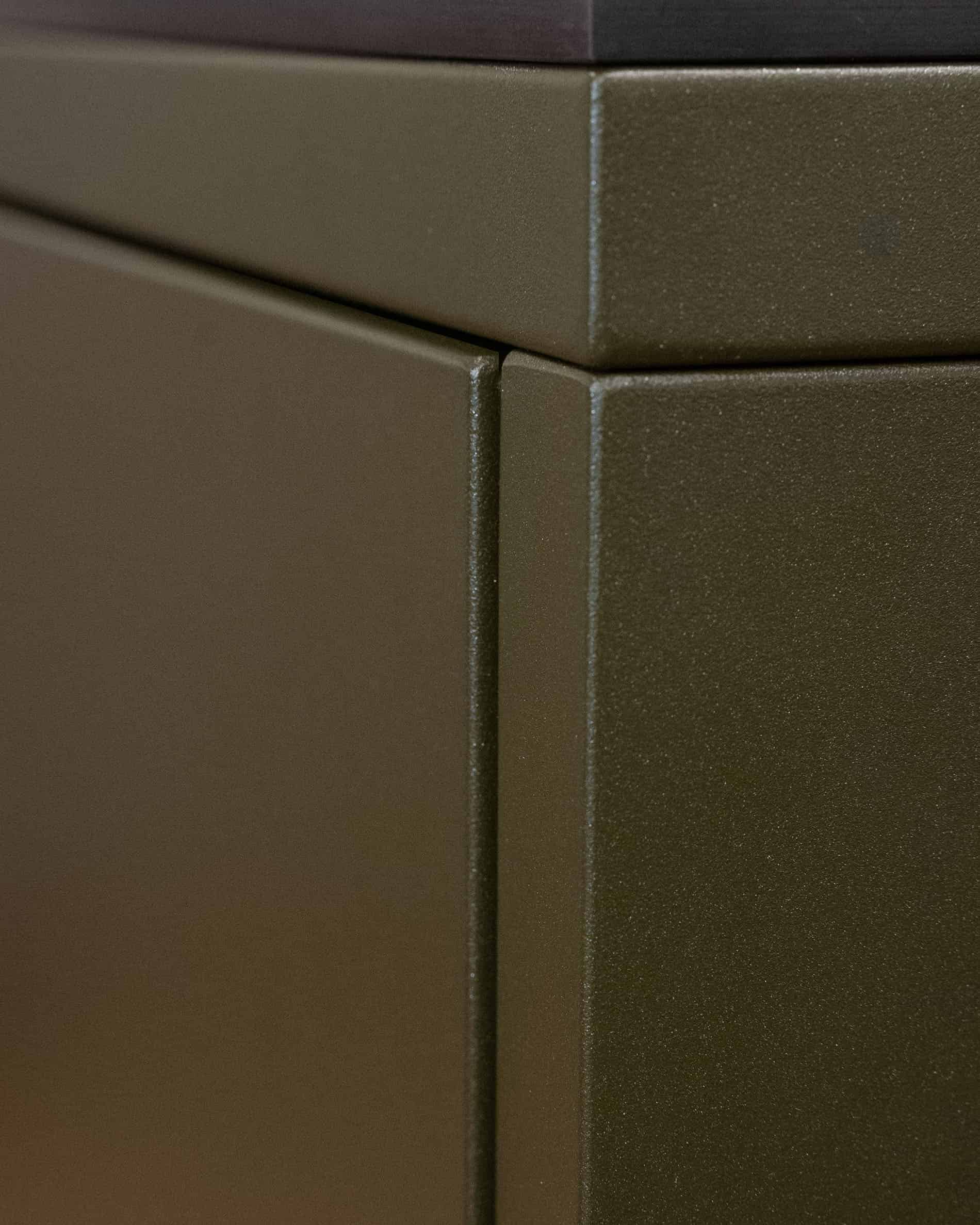 Detail van de afwerking van een pilotis buitenkeuken, met het samenspel van metalen panelen en de olijfgroene textuur van de voorzijde.